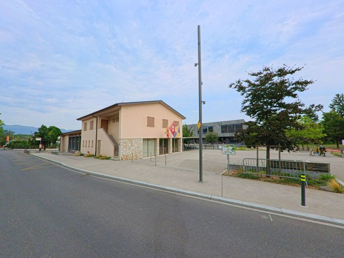 Vor einem modernen Platz in Chambesy (1292, Kanton Genf) steht ein Gebaeude mit Fahnen und Steinmauer im unteren Bereich.