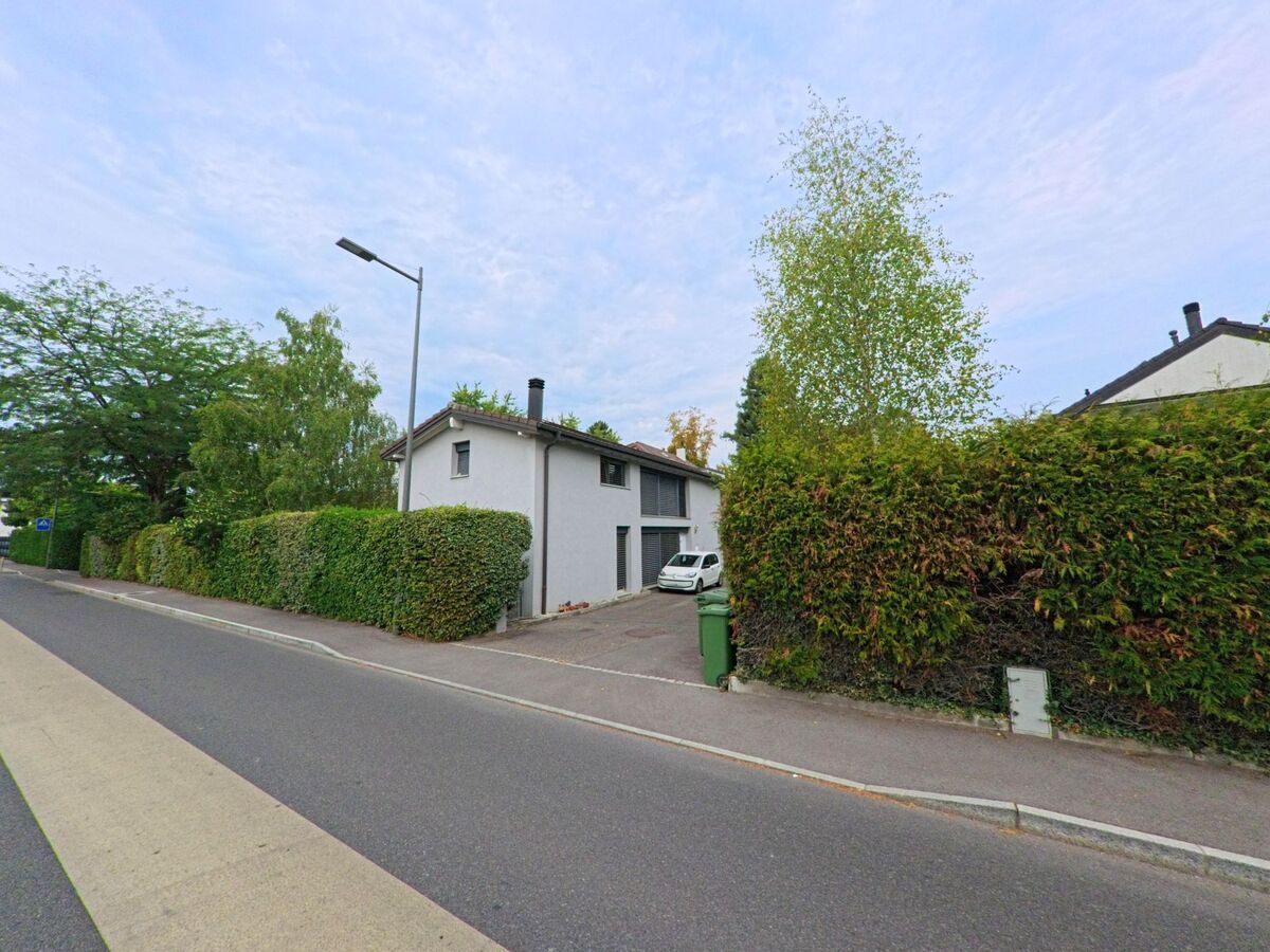 Ein weisses Wohnhaus mit Einfahrt und umgebenden Hecken steht an einer Strasse in Chambesy (1292, Kanton Genf).