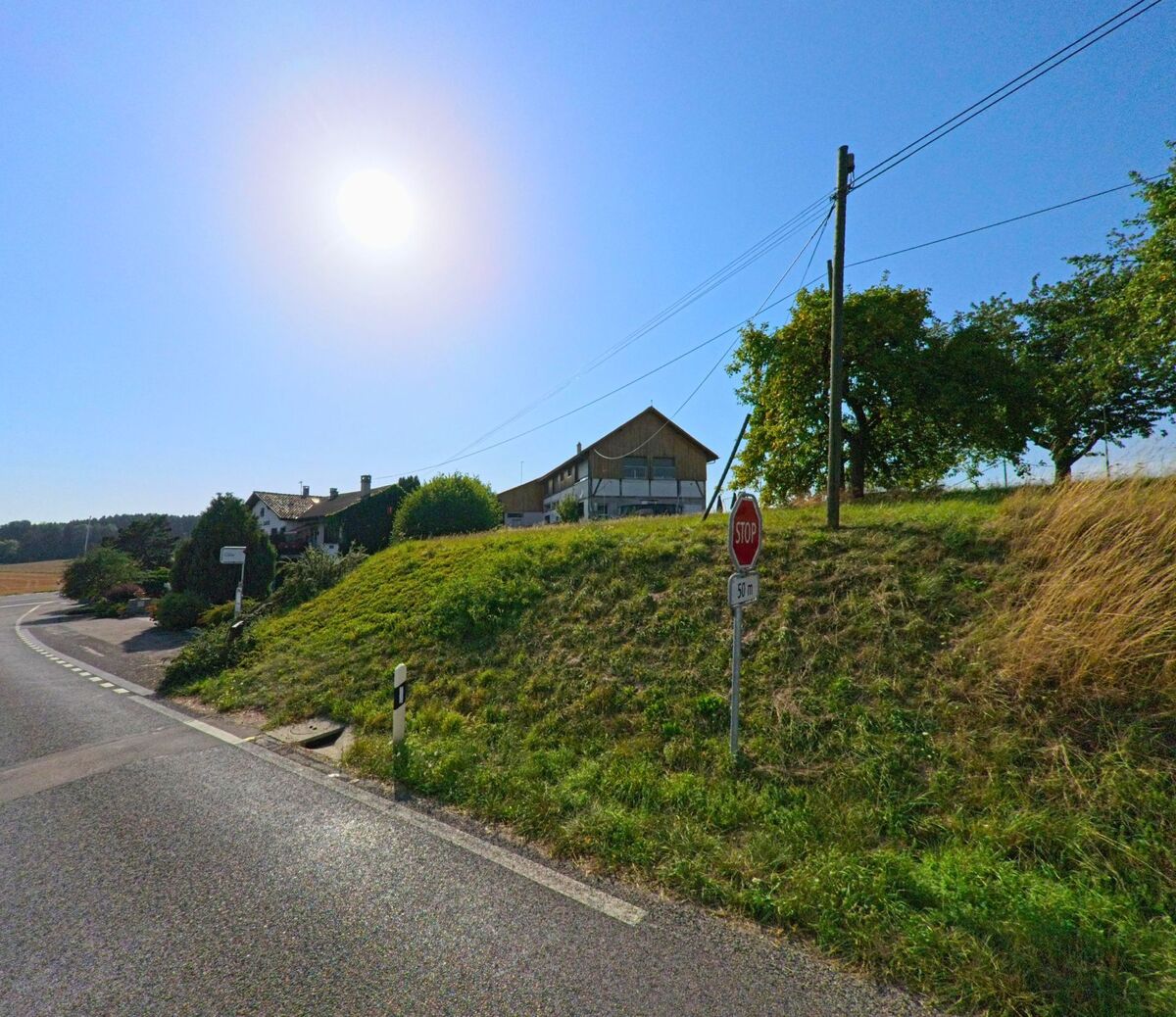 An einer Strassenkurve in Champtauroz (1537, Kanton Waadt) steht ein Stoppschild vor Wohnhäusern und einem grösseren Gebäude.