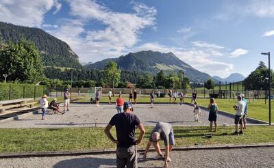 Mehrere Personen spielen Pétanque auf einem Kiesplatz mit Bergkulisse in Val de Charmey (1637, Kanton Freiburg) und zeigen gemeinsames Freizeitspiel.