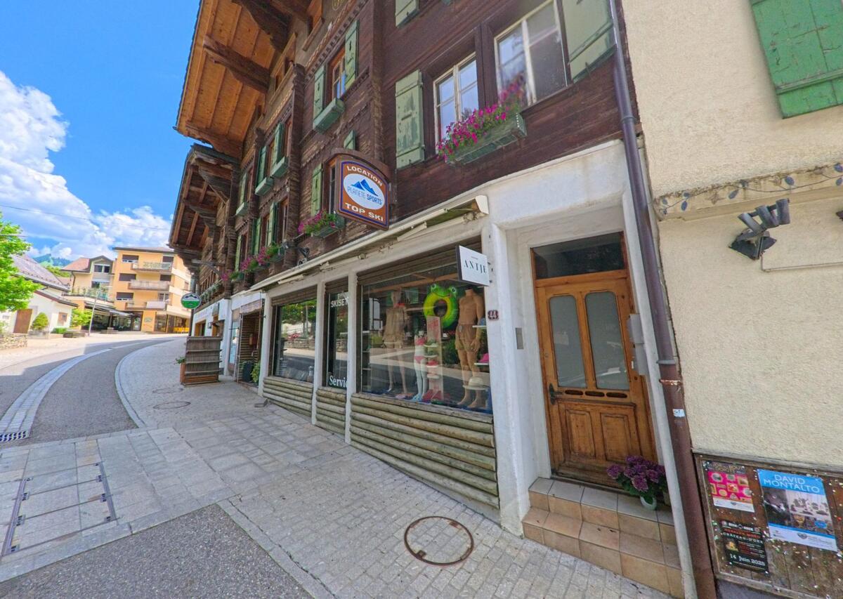 In Château-d'Oex (1660, Kanton Waadt) reiht sich ein Sportgeschäft mit traditionellen Holzfassaden an einer gepflasterten Altstadtgasse mit sanfter Steigung.