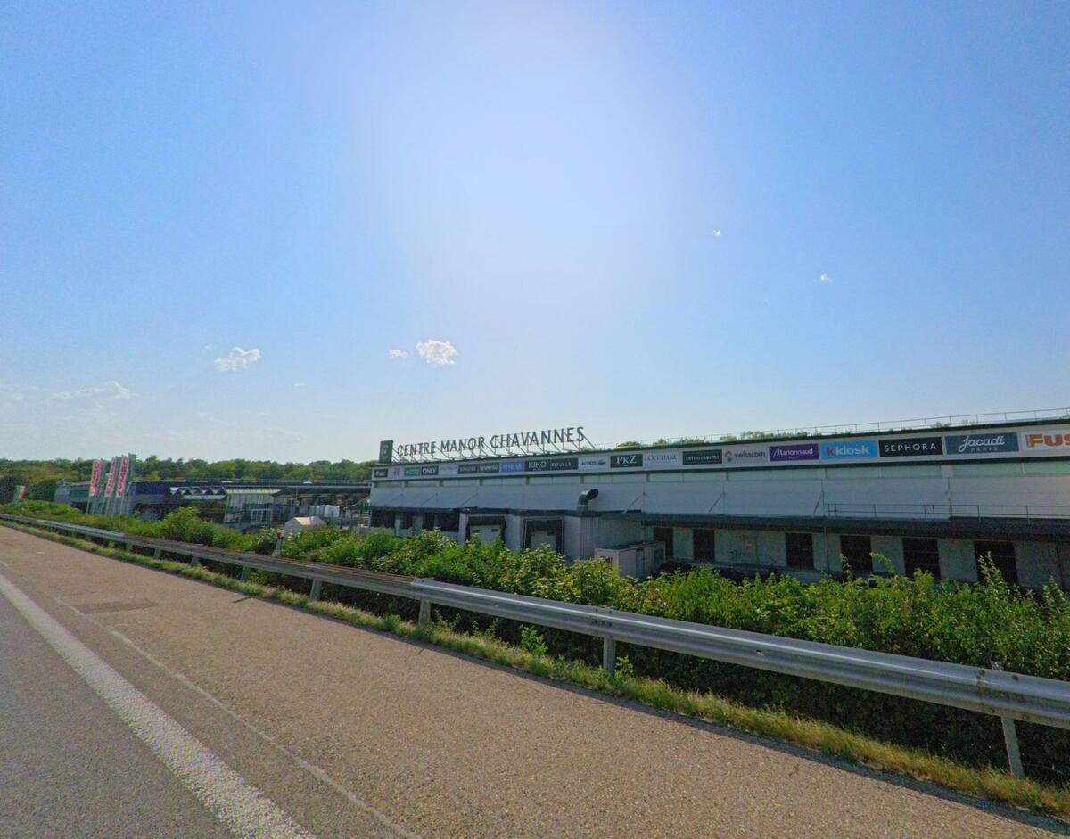 Das Einkaufszentrum „Centre Manor Chavannes“ liegt in Chavannes-de-Bogis (1279, Kanton Waadt) direkt an der Strasse unter strahlender Sonne.