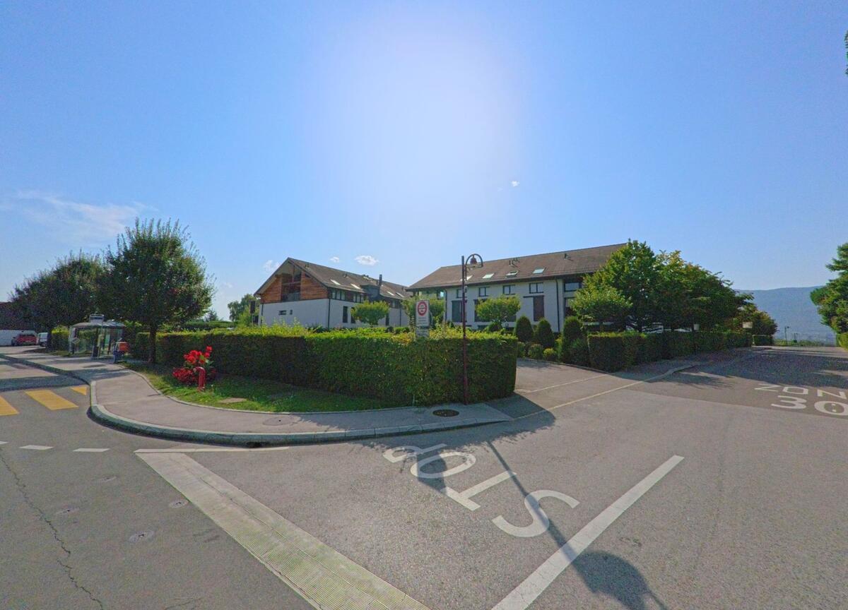 An einer verkehrsberuhigten Strasse mit Tempo-30-Zone stehen Mehrfamilienhäuser und eine Bushaltestelle in Chavannes-de-Bogis (1279, Kanton Waadt).