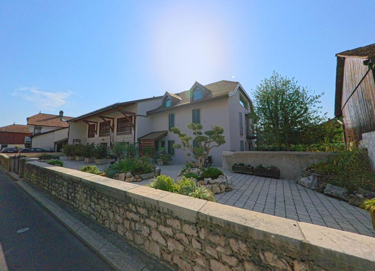 Ein modernisiertes Wohnhaus mit Gartenanlage und Steinmauer steht in Chavannes-de-Bogis (1279, Kanton Waadt) im Sonnenschein.