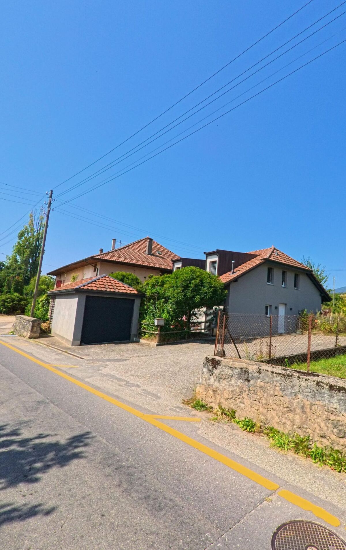 Am Dorfrand von Chavannes-le-Veyron (1148, Kanton Waadt) stehen Einfamilienhaeuser mit roten Daechern und kleinen Gaerten entlang einer ruhigen Strasse.