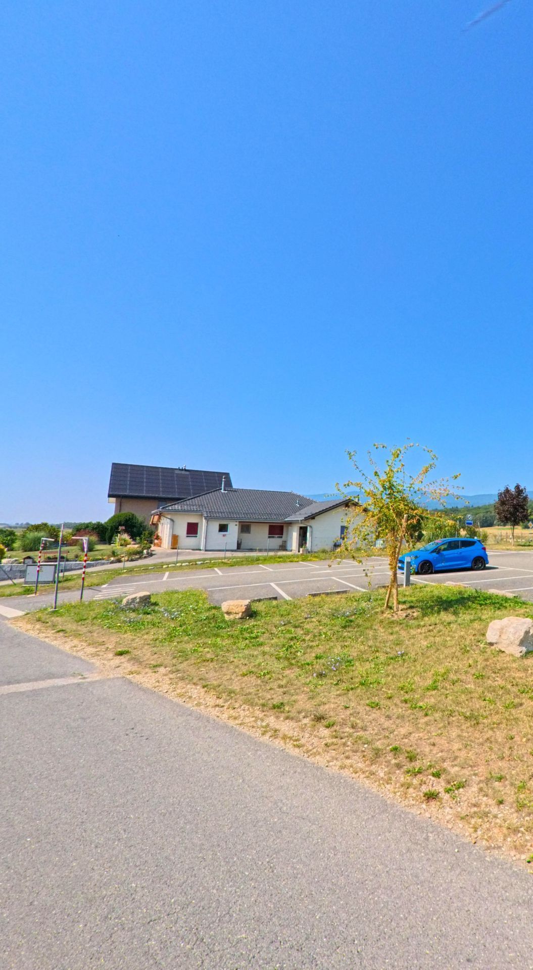 Am Ortsrand von Chavannes-le-Veyron (1148, Kanton Waadt) steht ein modernes Haus mit Solarpanels und angrenzendem Parkplatz unter blauem Himmel.