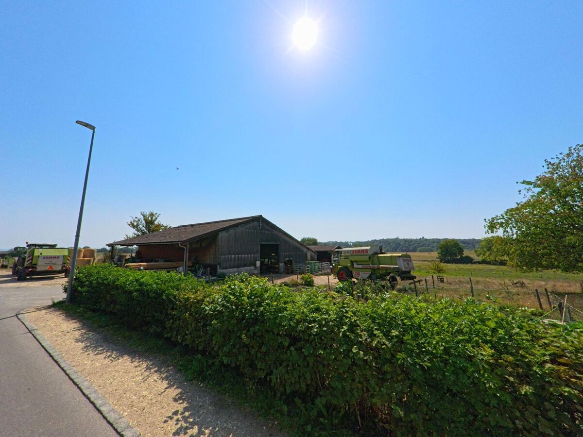 Ein Landwirtschaftsbetrieb in Chavannes-le-Veyron (1148, Kanton Waadt) zeigt unter strahlender Sonne Traktoren und Erntemaschinen neben einer einfachen Scheune.