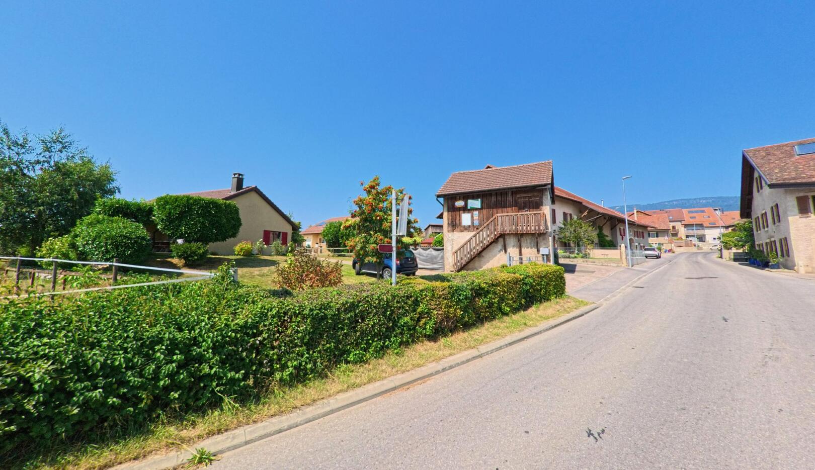 In Chavannes-le-Veyron (1148, Kanton Waadt) führt eine ruhige Strasse an gepflegten Einfamilienhäusern und einem kleinen Holzhaus mit Treppe vorbei.