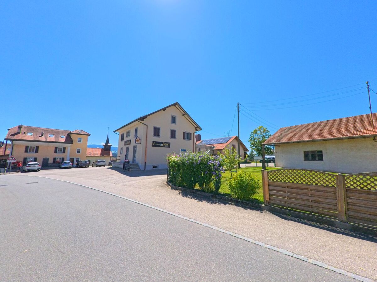 Im Zentrum von Chénens (1744, Kanton Freiburg) stehen mehrere Wohnhäuser und ein Gasthaus, im Hintergrund ist der Kirchturm sichtbar.