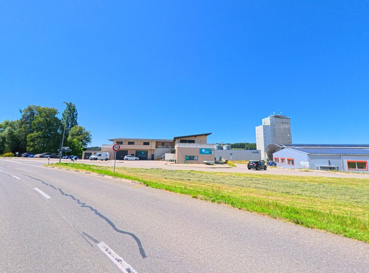 Am Ortseingang von Chénens (1744, Kanton Freiburg) stehen mehrere Industriegebäude und Lagerhallen, im Hintergrund ragt ein hoher Siloturm auf.