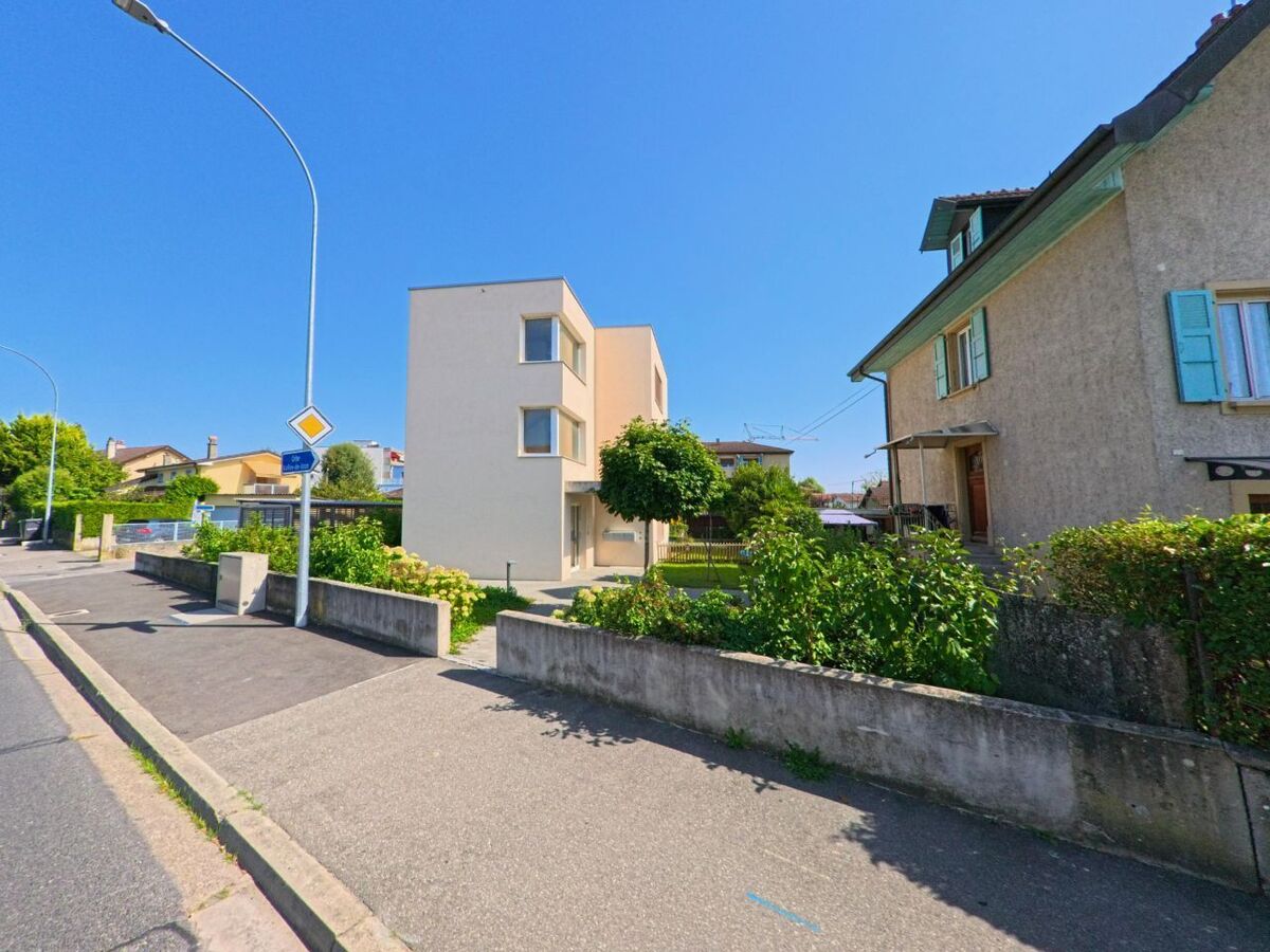 In Cheseaux-Noréaz (1400, Kanton Waadt) stehen moderne und traditionelle Wohnhäuser nebeneinander entlang einer ruhigen Strasse mit Vorgärten.