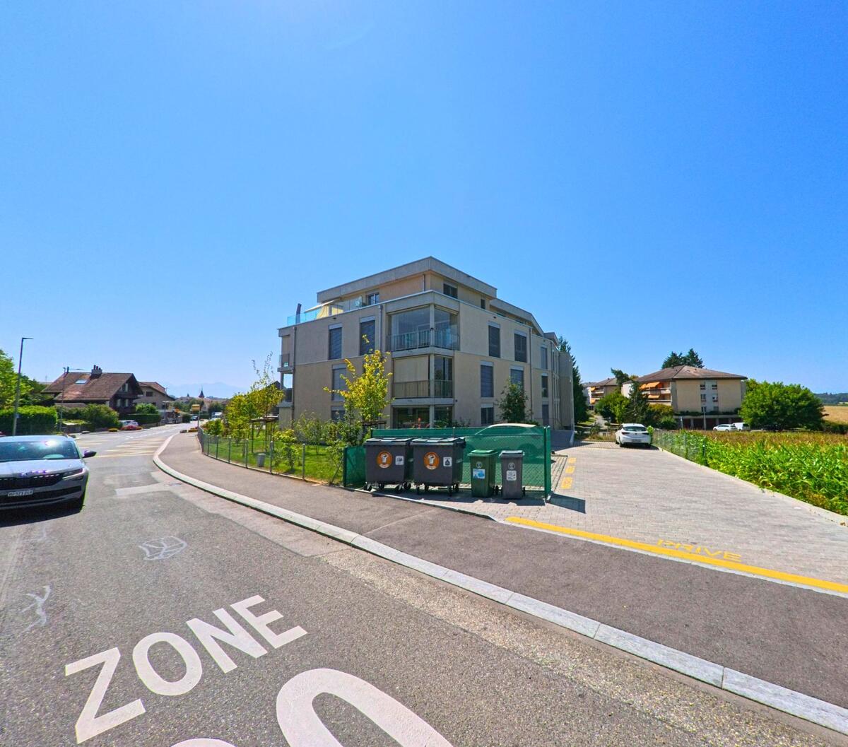 Ein modernes Wohnhaus in Cheseaux-sur-Lausanne (1033, Kanton Waadt) steht am Rand einer Strasse mit Tempo-30-Zone, umgeben von Feldern und weiteren Gebaeuden.