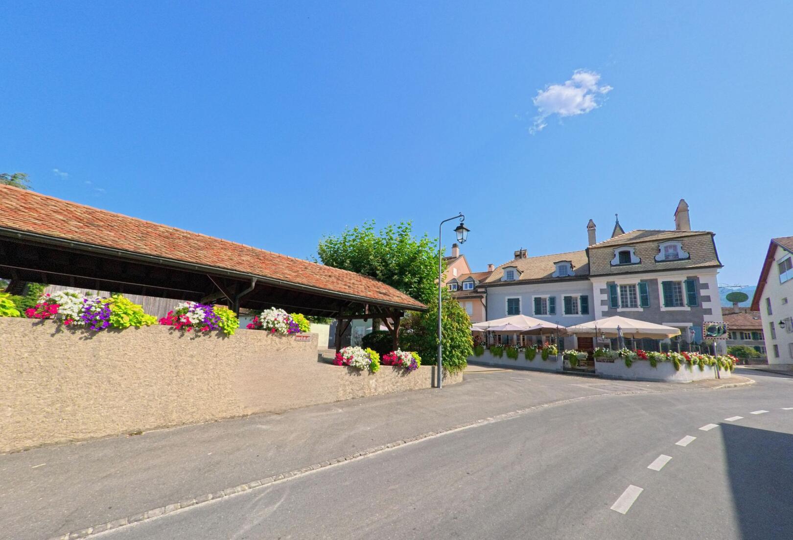 Im Zentrum von Chéserex (1275, Kanton Waadt) kontrolliert ein Kammerjaeger die Mauern nahe einem Gasthaus mit Blumenschmuck.