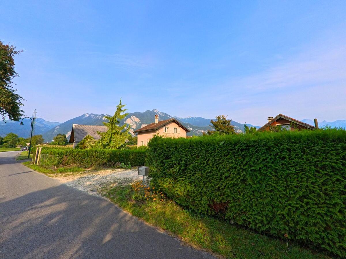 Hinter einer hohen Hecke in Chessel (1846, Kanton Waadt) sind Wohnhaeuser zu sehen, im Hintergrund erheben sich die Berge.