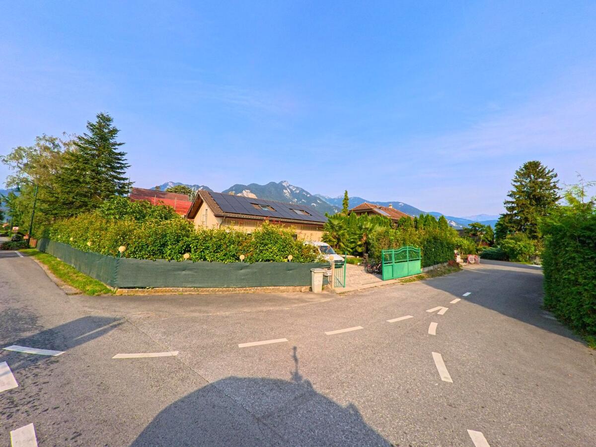 In Chessel (1846, Kanton Waadt) fuehrt eine kleine Strasse an Wohnhaeusern mit Solardach vorbei, dahinter erheben sich die Alpen.