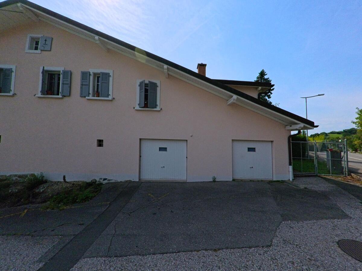 Ein helles Wohnhaus mit grauen Fensterläden und zwei Garagentoren steht in Chexbres (1071, Kanton Waadt) an einer ruhigen Strasse.