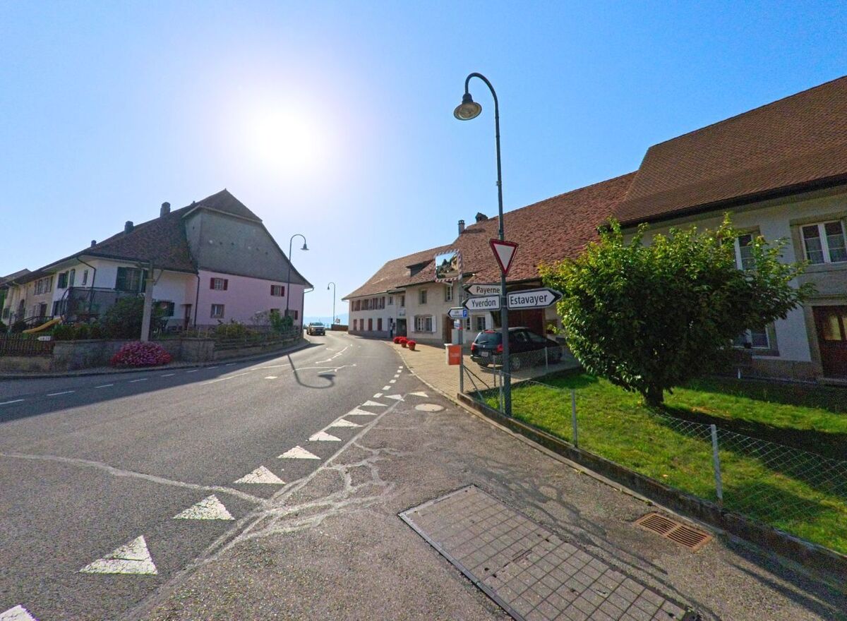 An einer Kreuzung in Cheyres-Chables (1474, Kanton Freiburg) weisen Wegweiser in Richtung Payerne, Yverdon und Estavayer, waehrend traditionelle Haeuser die Strasse saeumen.