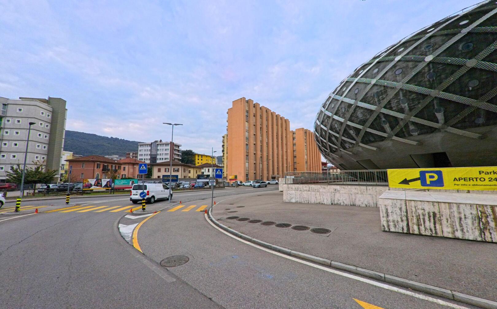 In Chiasso (6832, Kanton Tessin) zeigt sich eine moderne Strassenszene mit dem markanten runden Bau des Bahnhofsgebäudes und angrenzenden Wohnhäusern unter bewölktem Himmel.