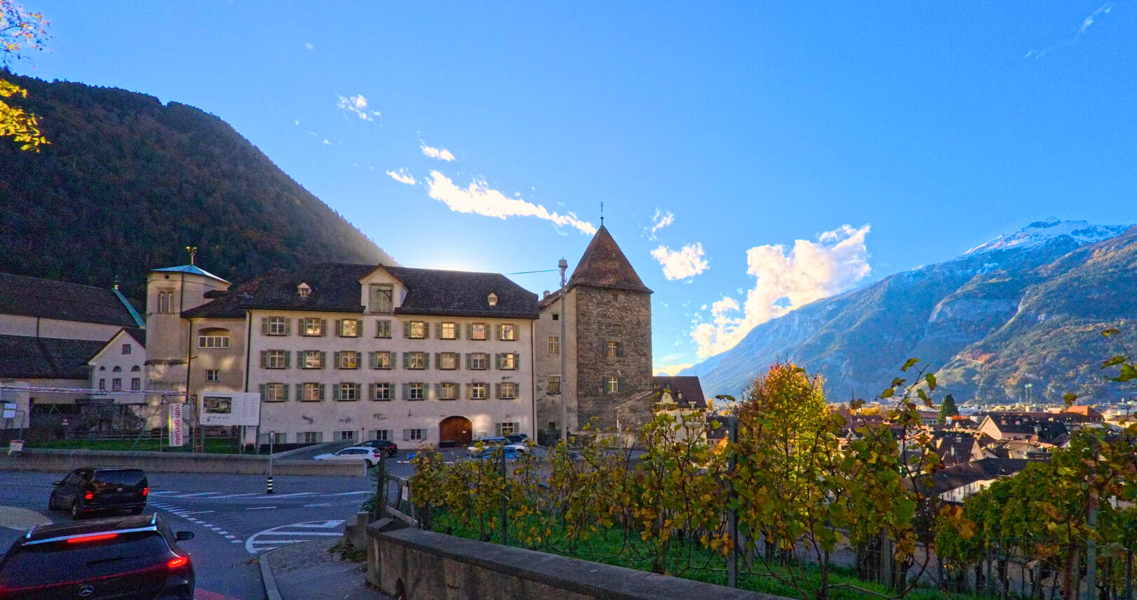 Ein historisches Gebaeude mit Turm steht an einer Strassenkreuzung vor alpiner Kulisse in Chur (7000, Kanton Graubünden).