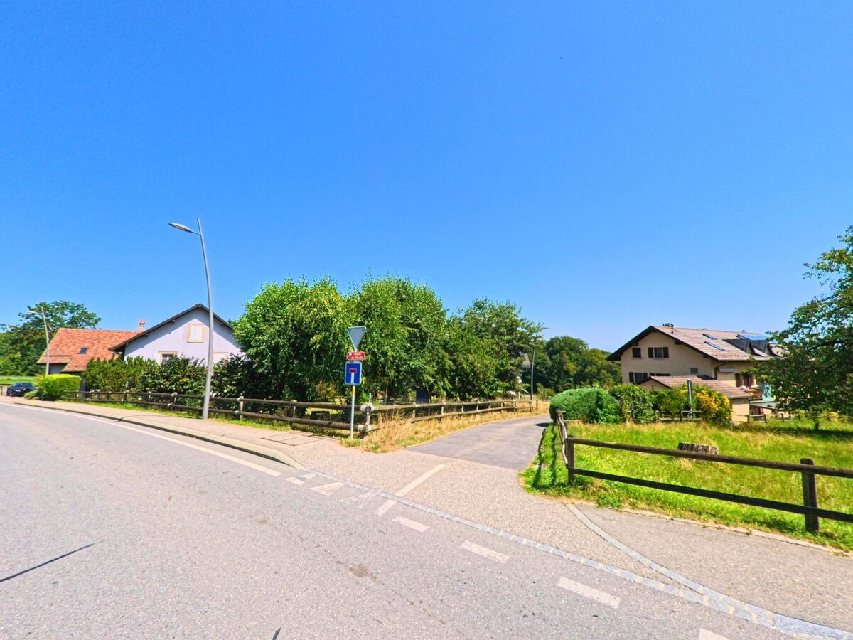 In Clarmont (1127, Kanton Waadt) zweigt ein schmaler Weg von der Hauptstrasse ab, gesäumt von Holzzäunen und umgeben von Wohnhäusern mit Gärten.