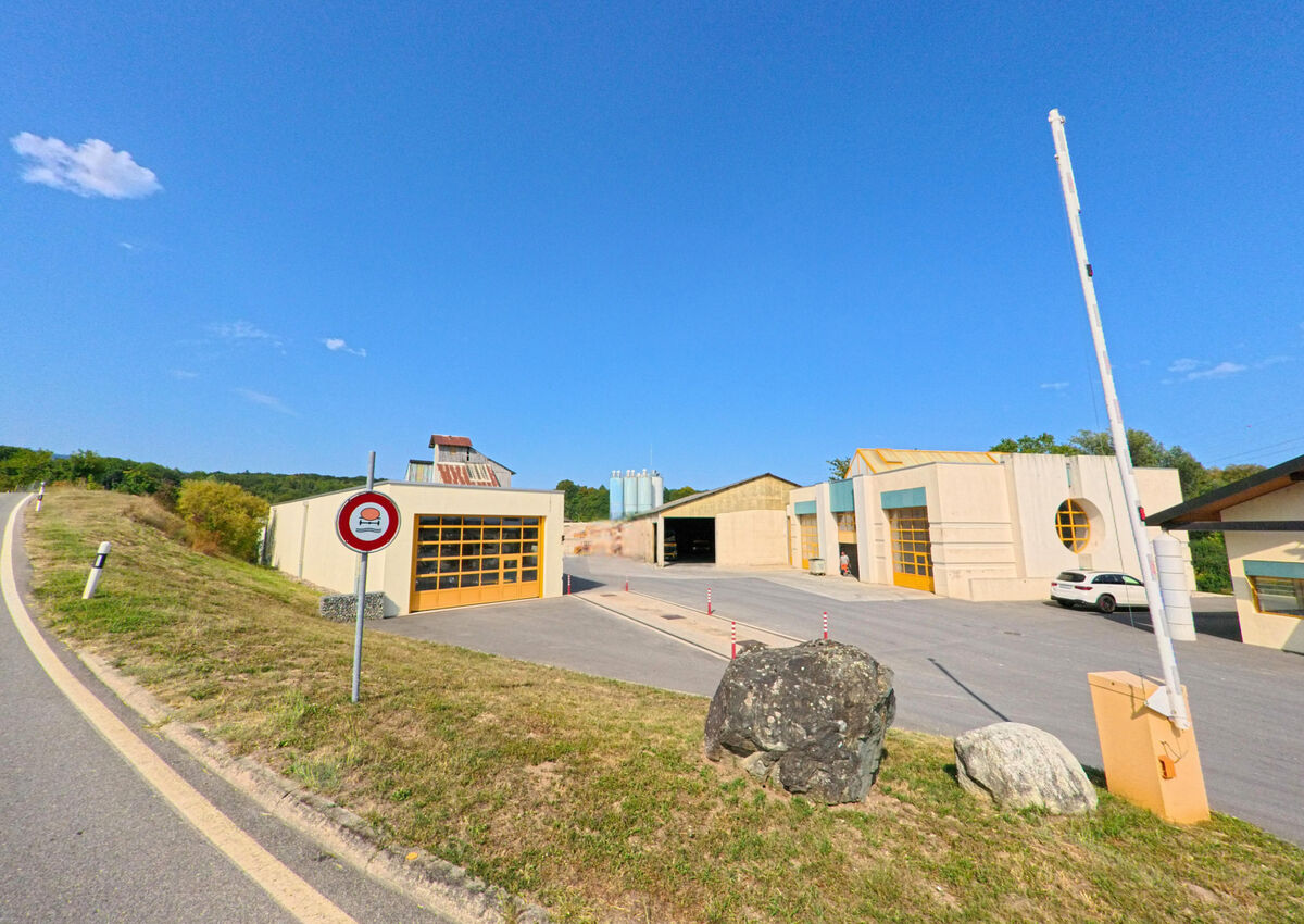 Am Ortsrand von Coinsins (1267, Kanton Waadt) stehen mehrere Gewerbegebaeude mit grossen Toren neben einer Zufahrtsstrasse.