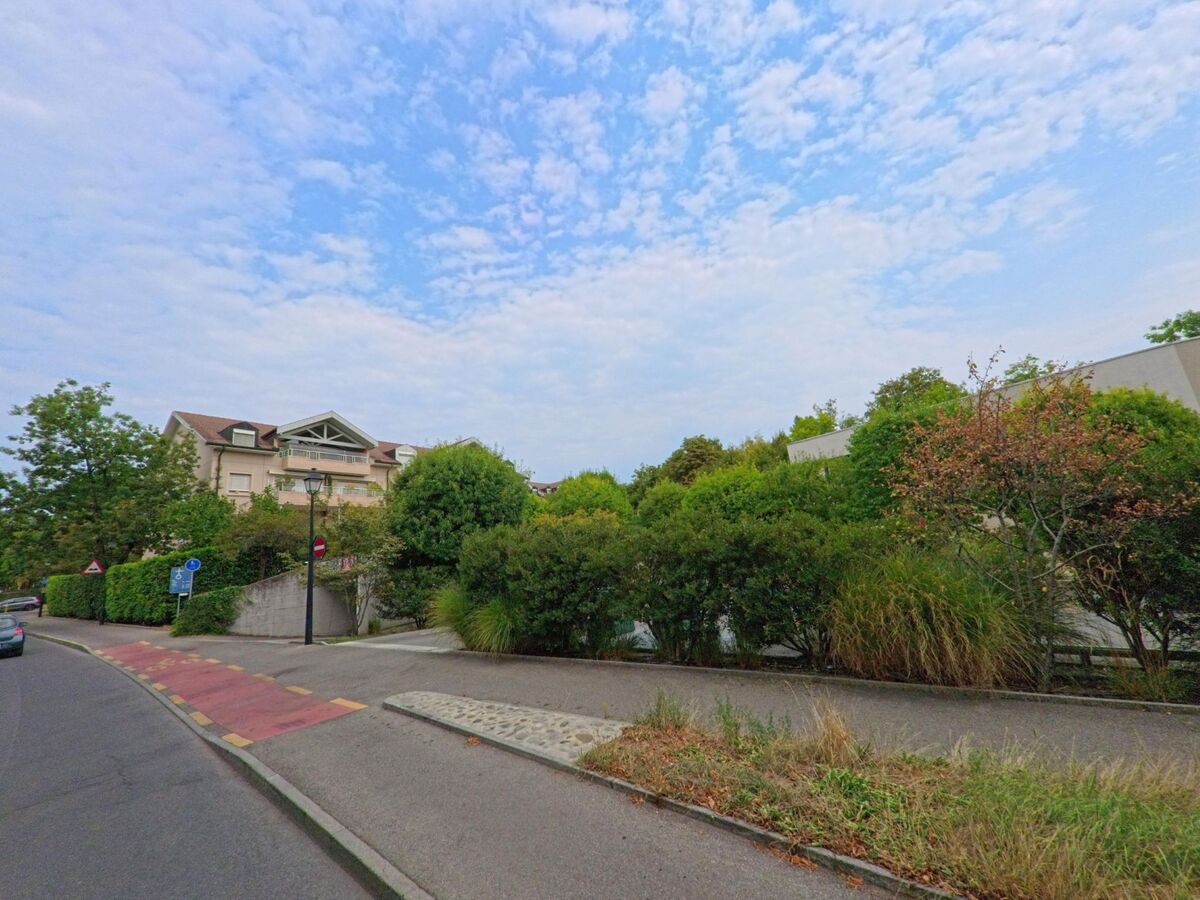 In Cologny (1223, Kanton Genf) verläuft eine Strasse mit Radweg und Fussgängern an modernen Wohnhäusern und Gärten vorbei.