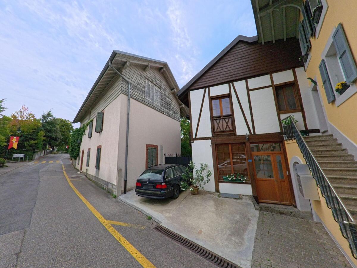 Zwischen traditionellen Wohnhaeusern mit Fachwerk und Holzverkleidung verläuft eine schmale Strasse in Commugny (1291, Kanton Waadt).