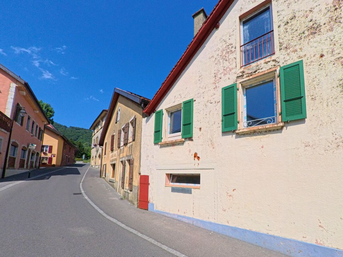 Eine schmale Strasse mit eng aneinandergereihten Wohnhaeusern in Concise (1426, Kanton Waadt) fuehrt leicht ansteigend in Richtung Waldrand.