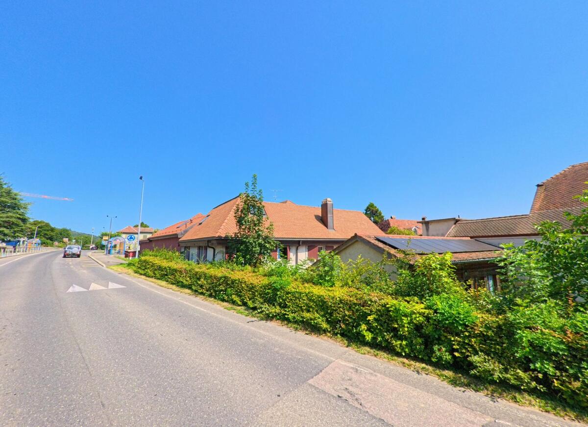Entlang der Hauptstrasse in Concise (1426, Kanton Waadt) stehen Haeuser mit roten Daechern, waehrend Autos die leicht ansteigende Fahrbahn passieren.