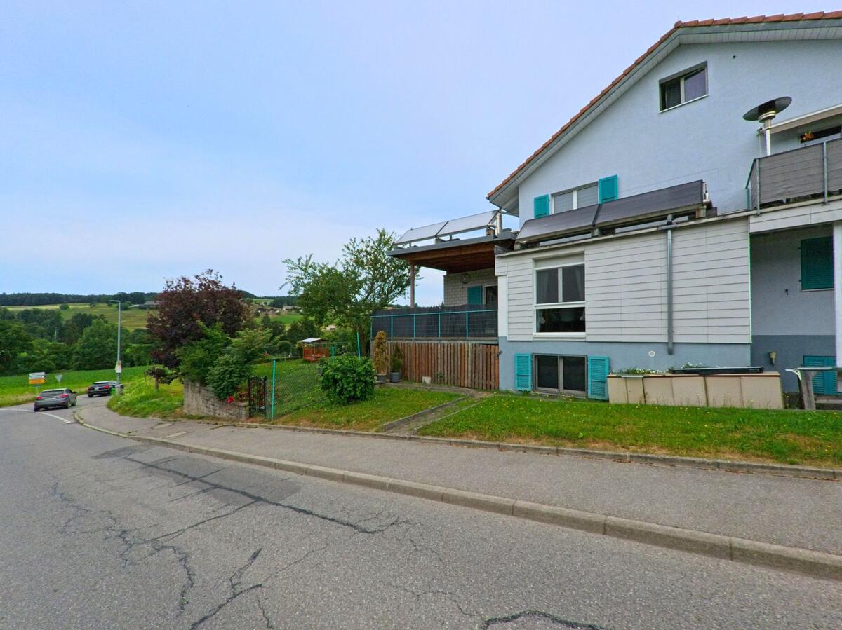 In Corminboeuf (Kanton Freiburg, PLZ 1720) steht ein modernes Wohnhaus mit Solarpanels am Hang, umgeben von Gärten und mit Blick auf die offene Landschaft.