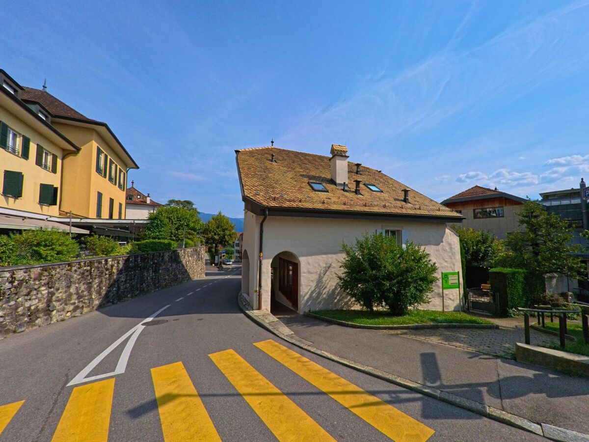 Ein kleines Haus mit schrägem Ziegeldach steht an einer kurvigen Strasse in Corseaux (1802, Kanton Waadt) neben einem Fussgängerstreifen.