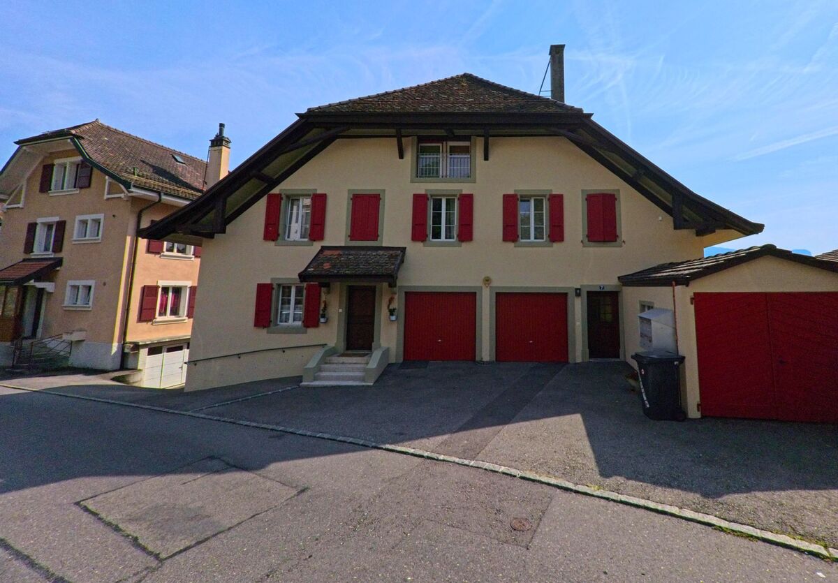 Ein traditionelles Wohnhaus mit roten Fensterläden und zwei Garagentoren steht an einer ruhigen Strasse in Corseaux (1802, Kanton Waadt).