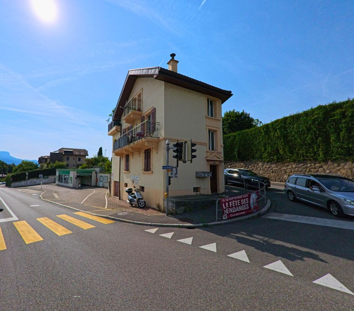 An einer Strassenkreuzung in Corseaux (1802, Kanton Waadt) steht ein schmales Wohnhaus mit Balkon neben einer Verkehrsampel.