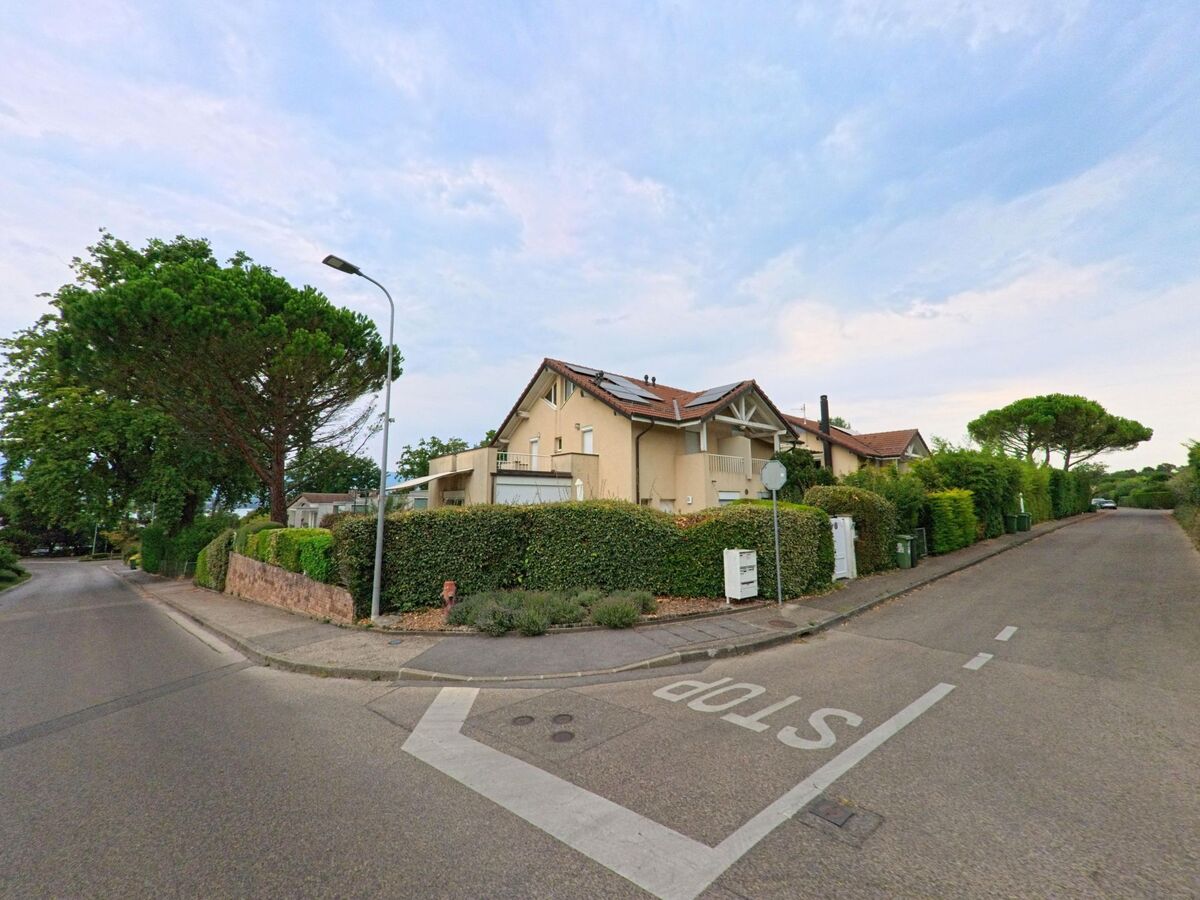 An einer Strassenecke in Corsier (1246, Kanton Genf) stehen Wohnhaeuser mit gepflegten Hecken und grossen Baeumen.
