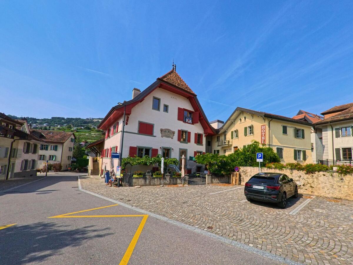 Ein traditionelles Gasthaus mit roten Fensterlaeden und ein Hotel praegen den gepflasterten Platz im Zentrum von Corsier-sur-Vevey (1804, Kanton Waadt).