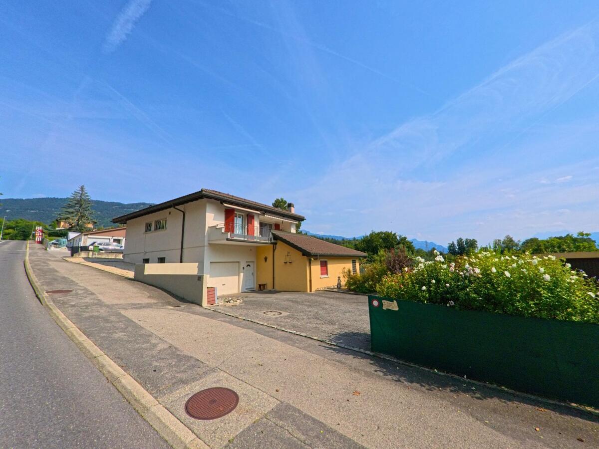 Ein Einfamilienhaus mit Garage und Balkon steht in Corsier-sur-Vevey (1809, Kanton Waadt) an einer leicht ansteigenden Strasse mit Blick auf die umliegenden Berge.