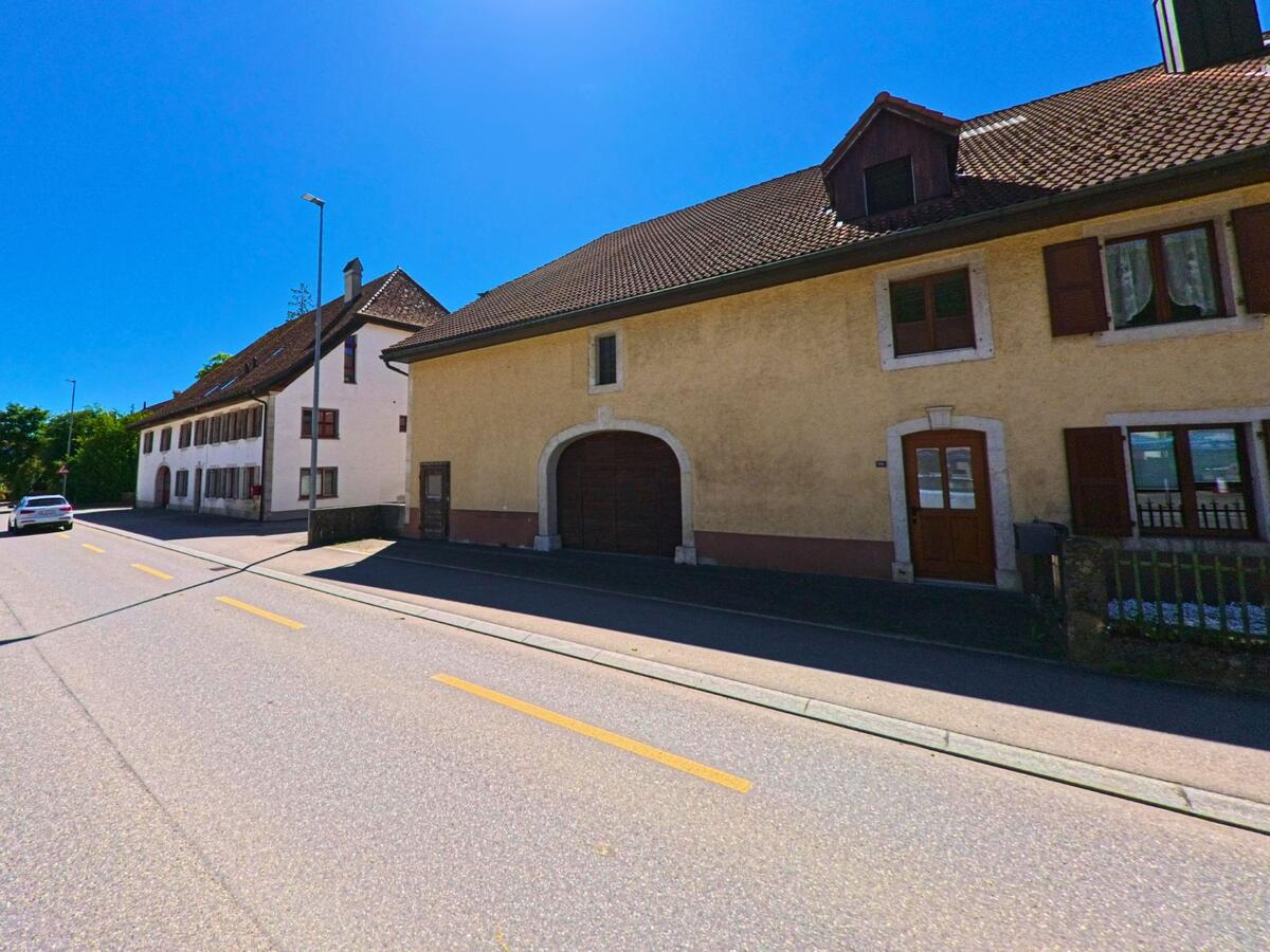 In Courtelary (2608, Kanton Bern) reihen sich traditionelle Wohnhäuser mit grossen Holztoren und Fensterläden entlang einer verkehrsarmen Strasse.