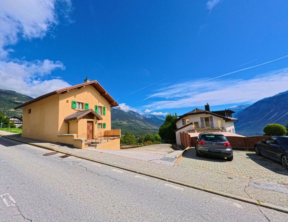 Am Hang in Crans-Montana (3974, Kanton Wallis) stehen Wohnhaeuser mit farbigen Fensterlaeden, von deren Lage sich ein weiter Blick ins Rhonetal und auf die Berge bietet.