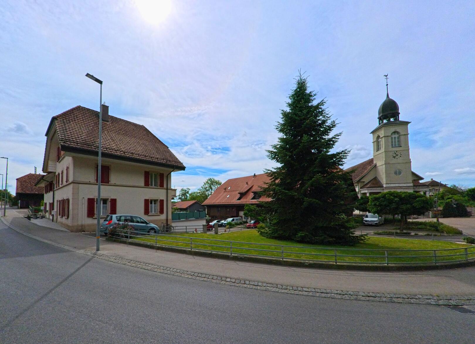 In Cressier (FR), 1785 im Kanton Freiburg steht eine reformierte Kirche mit markantem Turm neben traditionellen Wohnhäusern und einer gepflegten Grünfläche.