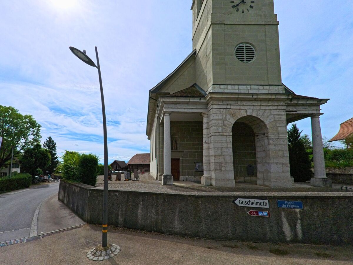 In Cressier (FR), 1785 im Kanton Freiburg steht die reformierte Kirche mit Uhrturm direkt an der Strasse Place de l’Église, von wo aus ein Weg nach Guschlmuth ausgeschildert ist.