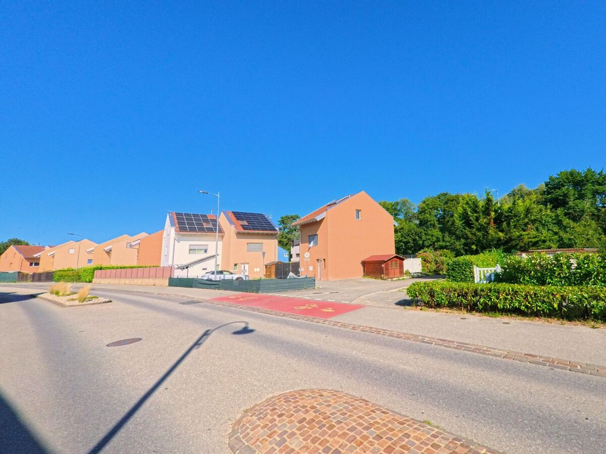 In Cudrefin (1588, Kanton Waadt) stehen moderne, orangefarbene Reihenhäuser mit Solarpanels auf den Dächern entlang einer ruhigen Strasse.