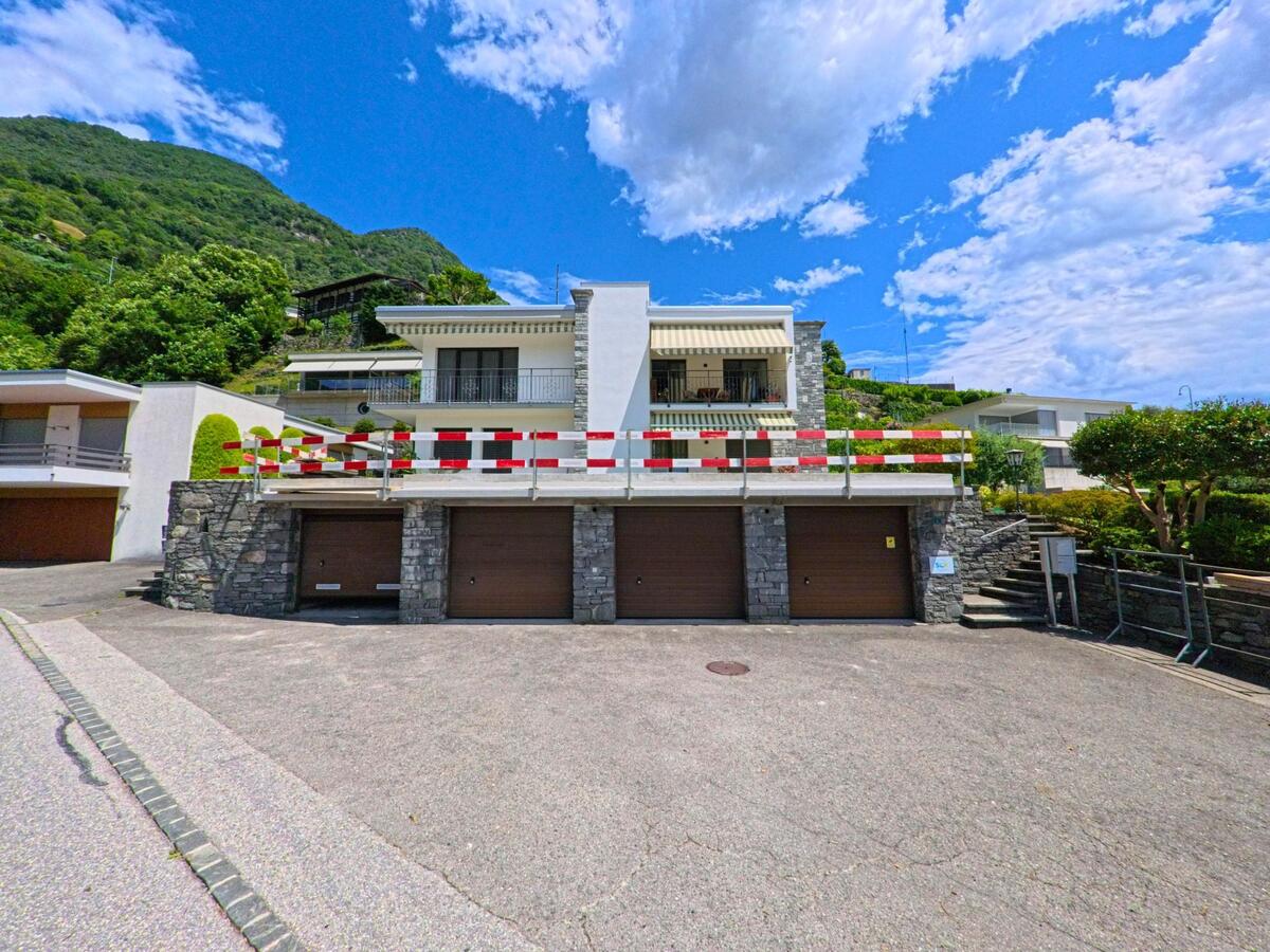 Ein modernes Wohnhaus mit Garagen und Steinfassade steht in Cugnasco-Gerra (6516, Kanton Tessin) am Hang unter blauem Himmel.