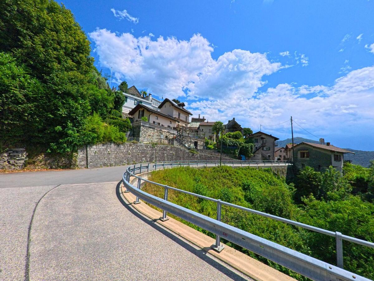 Eine kurvige Strasse führt in Cugnasco-Gerra (6597, Kanton Tessin) zwischen grüner Vegetation und alten Steinhäusern den Hang hinauf.