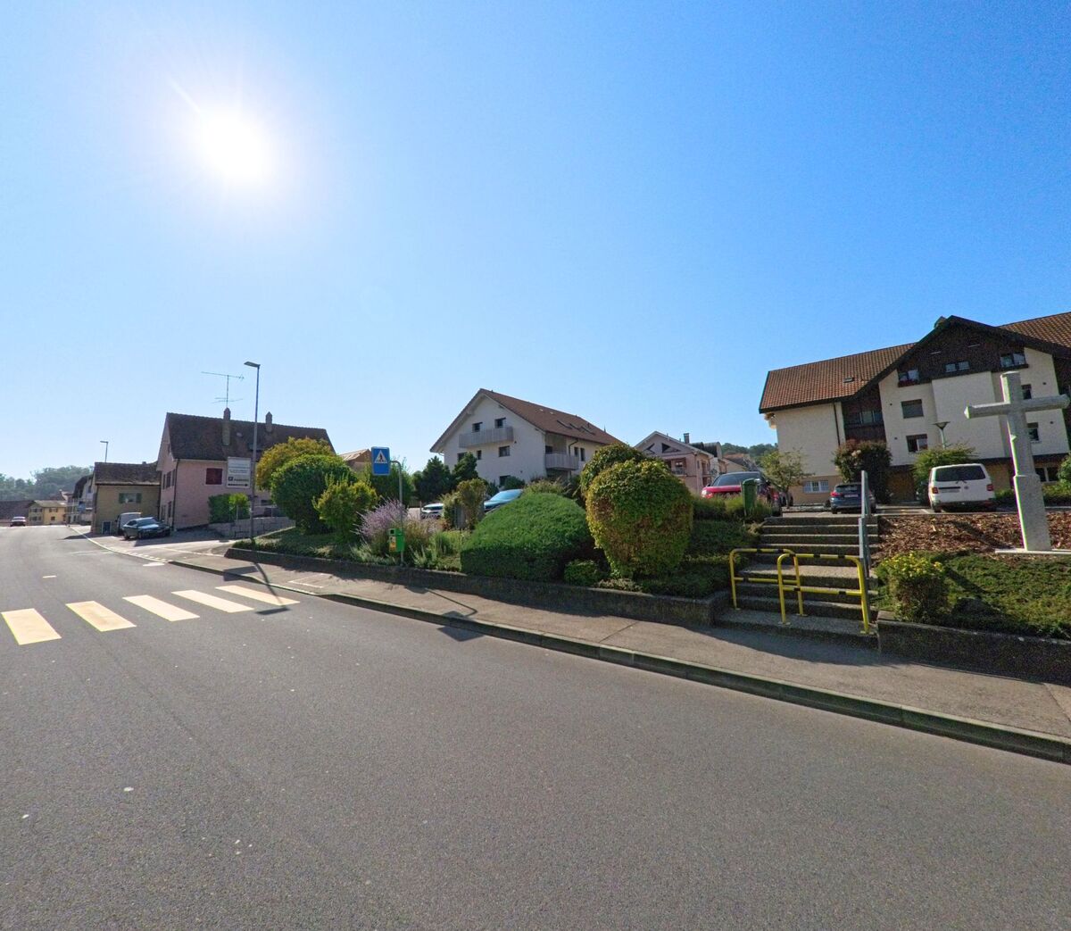 In Cugy (1482, Kanton Freiburg) fuehrt ein Fussgaengerstreifen zu einem Wohnquartier mit Einfamilienhaeusern und gepflegten Gaerten.