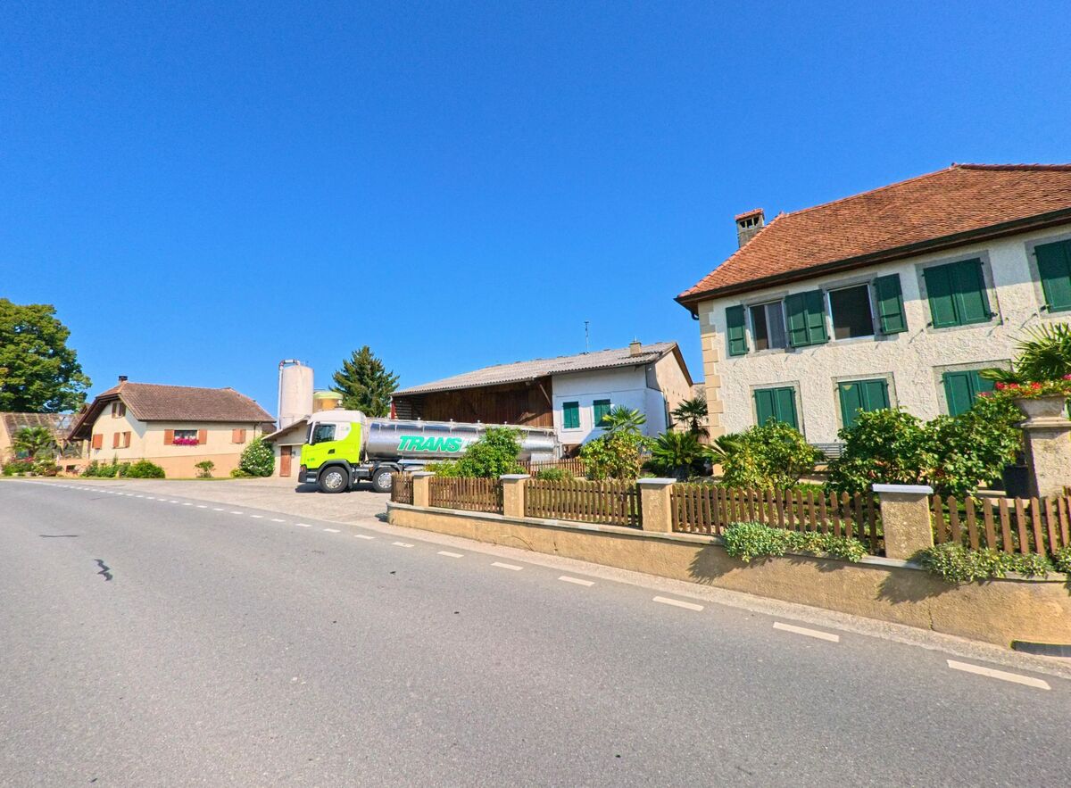 Vor traditionellen Wohnhaeusern in Cugy (1482, Kanton Freiburg) steht ein Lastwagen auf einem Hof neben einem Bauernhaus.