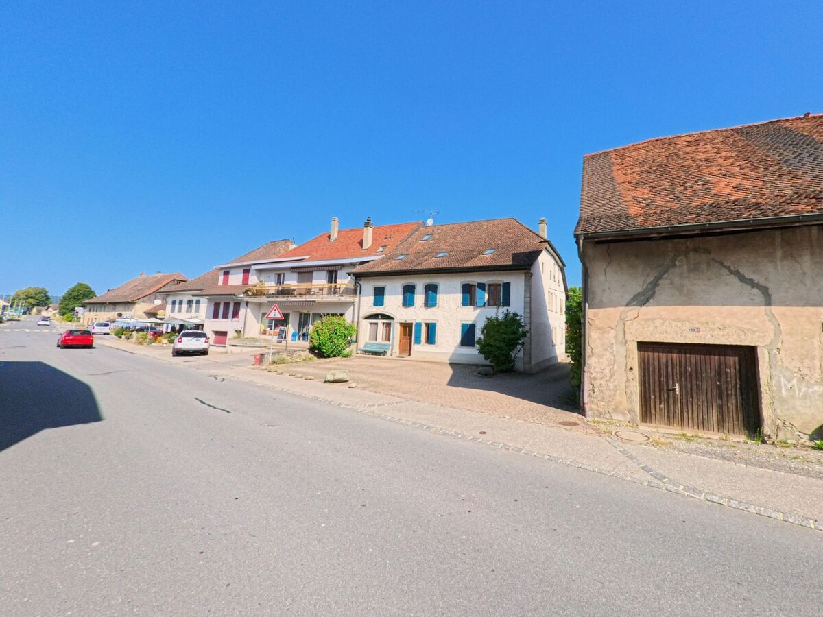 Entlang der Strasse in Cugy (1482, Kanton Freiburg) reihen sich traditionelle Wohnhaeuser mit farbigen Fensterlaeden und Balkonen.