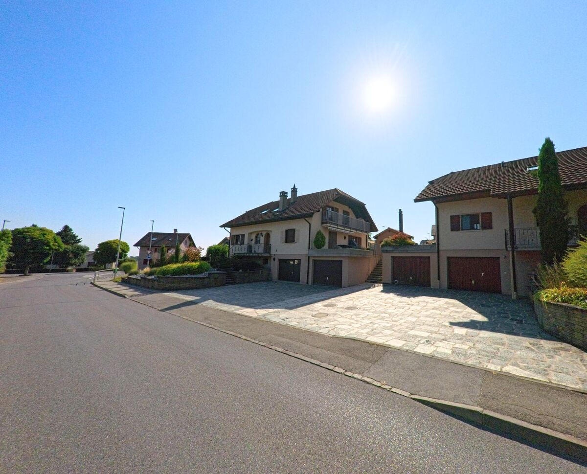 In Cugy (1483, Kanton Freiburg) stehen moderne Einfamilienhaeuser mit Garagen entlang einer ruhigen Strasse im Sonnenschein.