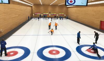 In der Curlinghalle in Luzern (6005, Kanton Luzern) spielen mehrere Teams Curling auf dem Eis. Zwei Teams in blauen und orangefarbenen Trikots ziehen ihre Steine in die Zielbereiche.