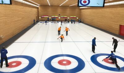 In der Curlinghalle in Luzern (6005, Kanton Luzern) spielen mehrere Teams Curling auf dem Eis. Zwei Teams in blauen und orangefarbenen Trikots ziehen ihre Steine in die Zielbereiche.