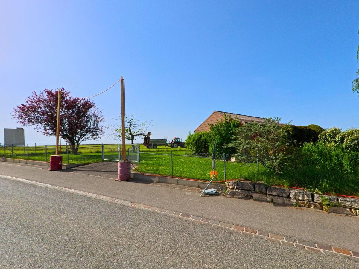 Am Ortsrand von Kaenerkinden (4447, Kanton Baselland) steht ein landwirtschaftliches Gelaende mit Wiese, Traktor, Holzhalle und einem auffälligen Baum vor weiter Landschaft.
